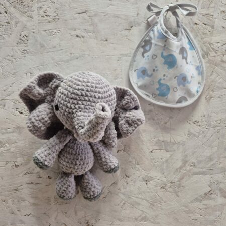 Doudou éléphant au crochet et petit bavoir naissance assorti posés sur une table.