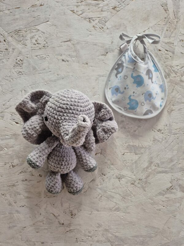 Doudou éléphant au crochet et petit bavoir naissance assorti posés sur une table.